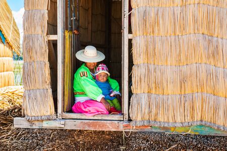 Titicaca lake, Puno, Peru - March, 20, 2017: Woman in traditional dresses with her child on Uros floating islands on Titicaca lake in Puno, Peruのeditorial素材