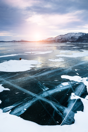 Cracked ice on the frozen lake. Beautiful winter landscape at sunsetの写真素材