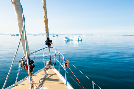 Yacht sailing among icebergs in Atlantic ocean in Greenlandの写真素材