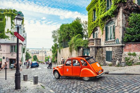 Paris, France - July, 21, 2019: Beautiful old street in Montmartre district in Paris, France. Orange retro car goes down the street.のeditorial素材