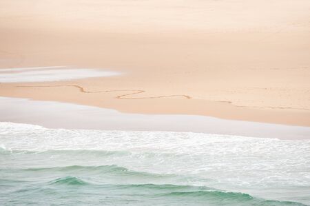 Waves on the beach and traces on the sand. Top view. Shore of Atlantic ocean in Algarve, Portugal. Abstract sea backgroundの写真素材