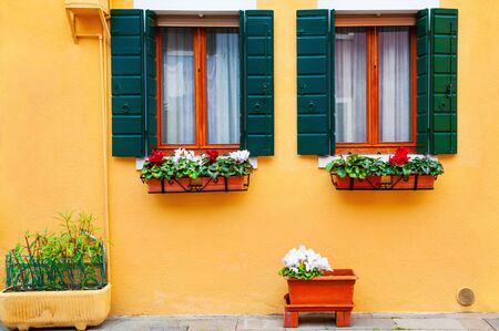 Windows with flowers on the yellow facade of the house. Colorful architecture in Burano island, Venice, Italy.の写真素材