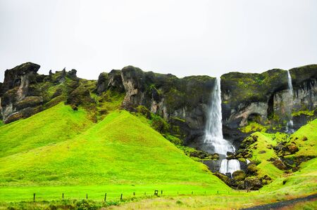 Beautiful waterfall in southern Iceland in foggy day. Green mountains and cloudy sky. Summer landscapeの写真素材