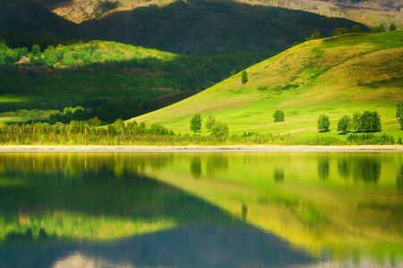 Green trees on the mountains and their reflections in the lake. Beautiful summer landscape. South Ural, Russiaの写真素材