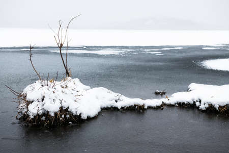 Ice with snow on the shore of lake during snowfall. Beautiful winter landscapeの写真素材