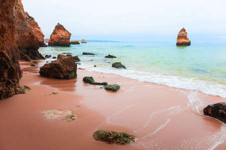 MIsty morning on the shore of Atlantic ocean in Algarve, Portugal. Red sand with turquoise water. Famous travel destinationの写真素材