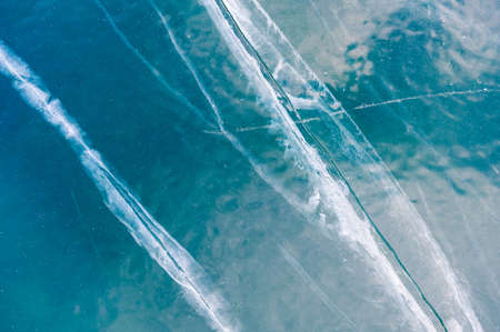 Texture of blue ice with cracks on the frozen lake. Macro image. Winter nature background