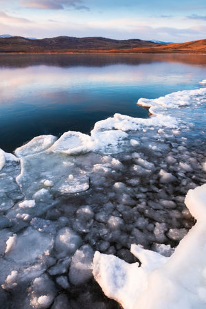 Ice on the frozen lake at sunset. Mountains and sky are reflected in the ice surface of the lake....