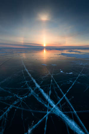 Baikal lake in winter with transparent cracked blue ice. Solar halo effect at sunrise. Baikal, Siberia, Russia. Beautiful winter landscape.の写真素材