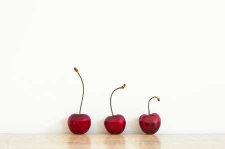 Three red ripe cherry on the table. White wall in the background. Vintage filter. Summer fruits nature backgroundの写真素材