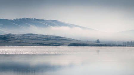 Beautiful lake in misty morning. Mountains reflected in the calm water surface. Autumn landscape....