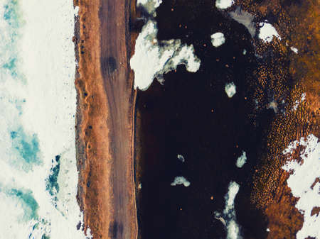 Melting ice on the lake and dirty road in countryside. Aerial drone view. Abstract anture backgroundの写真素材