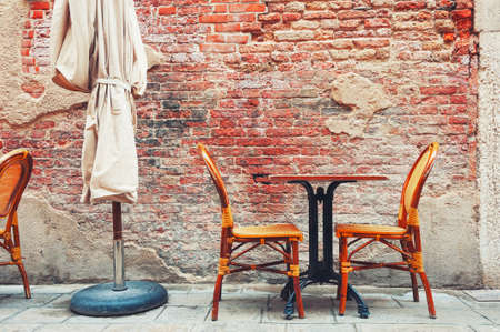 Cafe on the street in Venice, Italy. Chairs and table against the old brick wall of the house.の写真素材