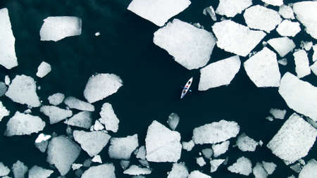 Kayak sailing between ice floes on the lake. Aerial drone view. abstract nature background. Baikal lake, Siberia, Russia. spring landscapeの写真素材