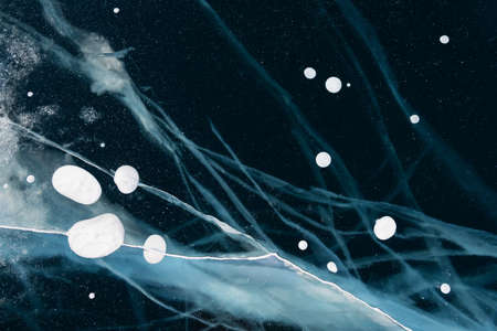 Transparent blue ice with cracks and bubbles on Baikal lake in winter. Abstract winter background....