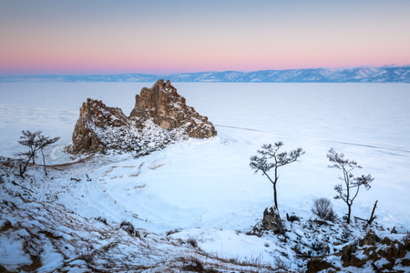 Frozen Baikal lake with snow in winter. Shamanka rock on Olkhon island at sunrise. Baikal, Siberia, Russia. Beautiful winter landscapeの写真素材