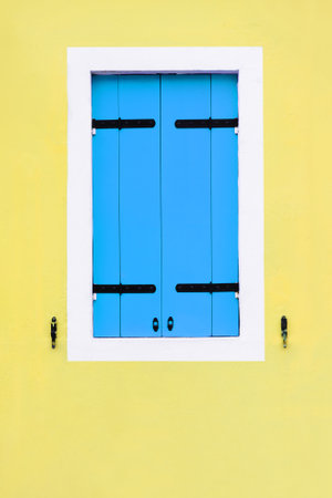 Yellow painted facade of the house and window with blue shutters. Colorful architecture in Burano island, Venice, Italy.の写真素材