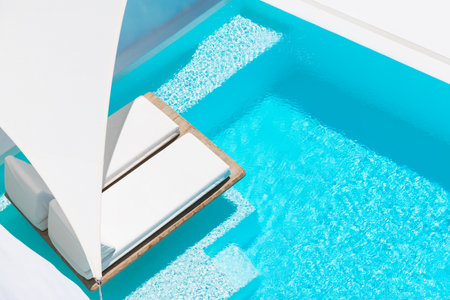 Luxury swimming pool with blue water and white chaise lounges. Santorini island, Greece. Travel and...