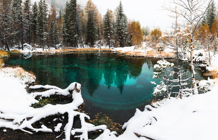 Blue geyser lake in autumn forest during snowfall. Altai mountains, Siberia, Russia. Lake with blue water and white snow. Autumn landscapeの写真素材