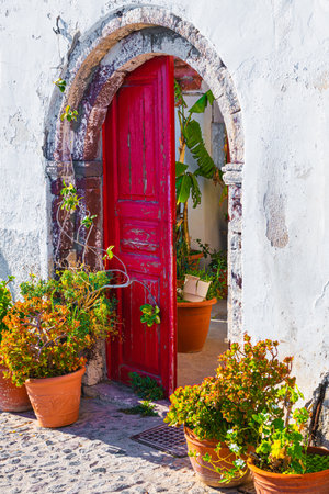 Traditional greek architecture in Oia village, Santorini island, Greece. Red wooden door with flowersの写真素材