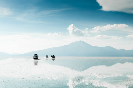 Off-road cars driving on Salar de Uyuni salt flat in Bolivia. Sky and mountains are reflected in the water surface.の写真素材