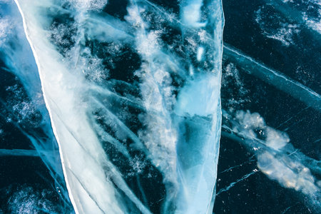 Transparent blue ice with cracks on Baikal lake in winter. Abstract winter nature background.