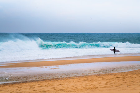 Surfer with surfboard standing on the ocean beach and waiting for the big wave. Atlantic ocean,...