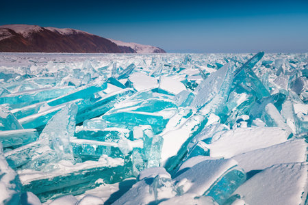 Transparent ice floes with snow on Baikal lake at sunset. Baikal, Siberia, Russia. Winter landscape