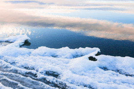 Ice on the shore of lake in winter. Clouds and sky are reflected in the water. Winter nature...