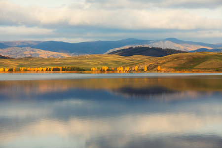Lake in the autumn mountains. Yellow trees and mountains are reflected in the lake at sunrise. Beautiful autumn landscape.の写真素材