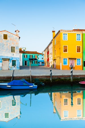 Colorful architecture in Burano island, Venice, Italy. Yellow house with blue shutters and blue boat on the canal.の写真素材