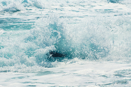 Waves on the beach in windy day. Sea foam splash close up. Aegean sea, Santorini island, Greece.