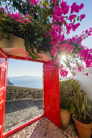 Beautiful patio with red door and blooming pink flowers. Santorini island, Greece. Travel and summer vacationsの写真素材