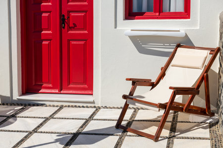 White architecture in Santorini island, Greece. Red painted door and window of the house. Chaise lounge on the terrace.の写真素材