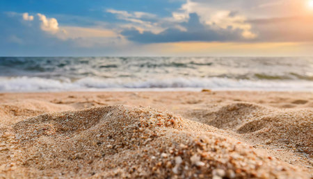 A close-up view of golden sand with a blurred background of ocean waves and a vibrant sunset sky.の写真素材
