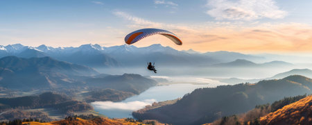 A paraglider soars above a stunning alpine lake at sunrise, mountains in the background. Breathtaking scenery.の写真素材