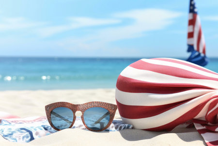 Wooden sunglasses rest on a red and white striped towel on a sandy beach, with ocean in background. Perfect summer scene!の写真素材