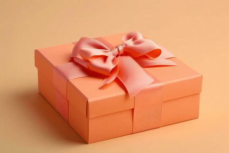 A close up of a peach gift box with a big pink bow, on a peach background.の写真素材