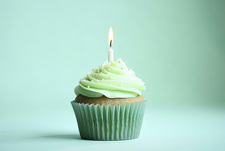 A single cupcake with a lit candle on top, frosted with green buttercream and sprinkled with pink...