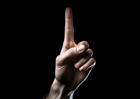 A close-up image of a hand with the index finger pointed up, isolated on a black background. The...