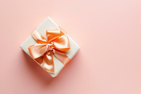 A white gift box with a peach ribbon bow on a pink background. The image is minimalist and elegant, with a focus on the gift box and ribbon.の写真素材