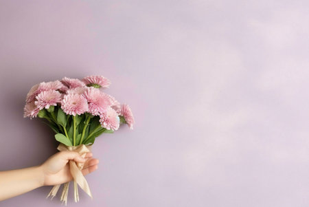 A hand gently holds a small bunch of light pink flowers against a pale purple background.の写真素材
