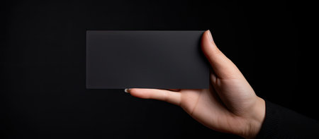 A blank black card being held by a hand against a dark background, perfect for mockup and design purposes.の写真素材