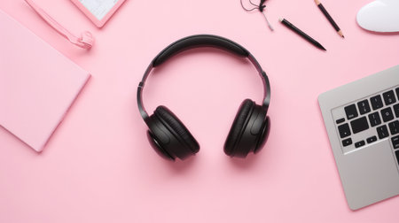 Black headphones on a pink desk with a laptop, notebooks, and pens. Minimalist and modern desk setup.の写真素材