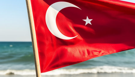 A close-up of the Turkish flag waving in the wind, with a blurred background of the sea and beach.の写真素材
