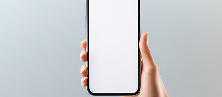 A close-up image of a hand holding a smartphone with a blank white screen. The background is a...