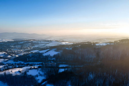 Stunning aerial shot of a snow-covered winter landscape. The sun sets over the hills, casting a warm glow.の写真素材