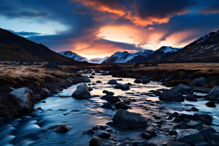 A breathtaking sunset paints the sky with vibrant colors over a serene river flowing through a snowy mountain valley.の写真素材