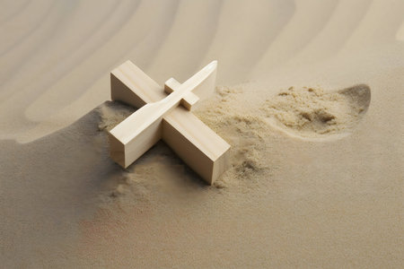 A simple wooden cross rests in the sand, evoking themes of faith and reflection.の写真素材