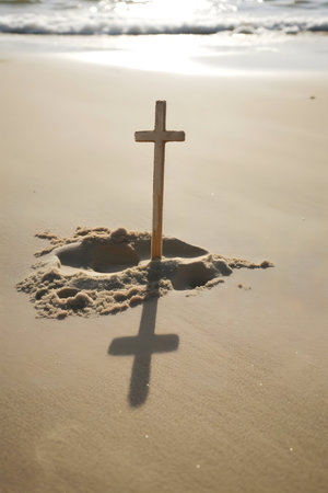 Wooden cross planted in beach sand, casting a long shadow. Sunrise or sunset. Peaceful scene.